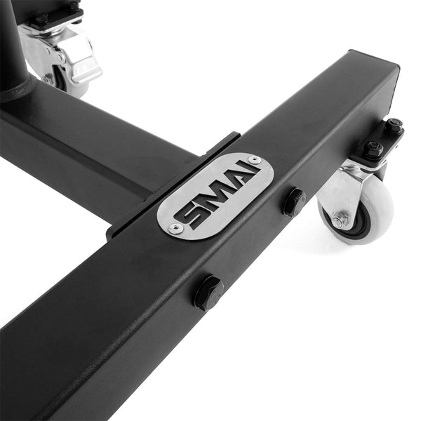 Close-up of the Bumper Plate Storage Stacker with Wheels, featuring a black metal frame equipped with wheels. A silver plate is affixed to the frame, engraved with the letters "SMAI." The photo showcases its robust construction and optimal design for bumper plate storage, offering superior mobility features.