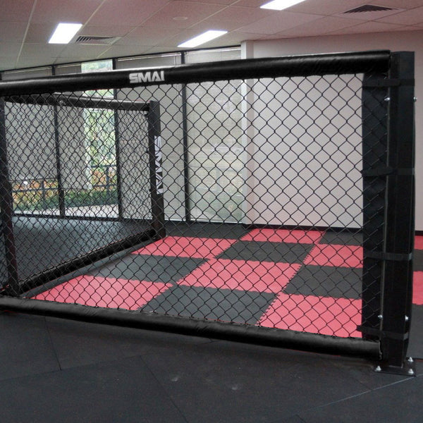 A black SMAI MMA Cage Panel Pack equipped with reinforced cage mesh stands in a gym, paired with a red and black checkered mat floor, set against a backdrop of glass windows.