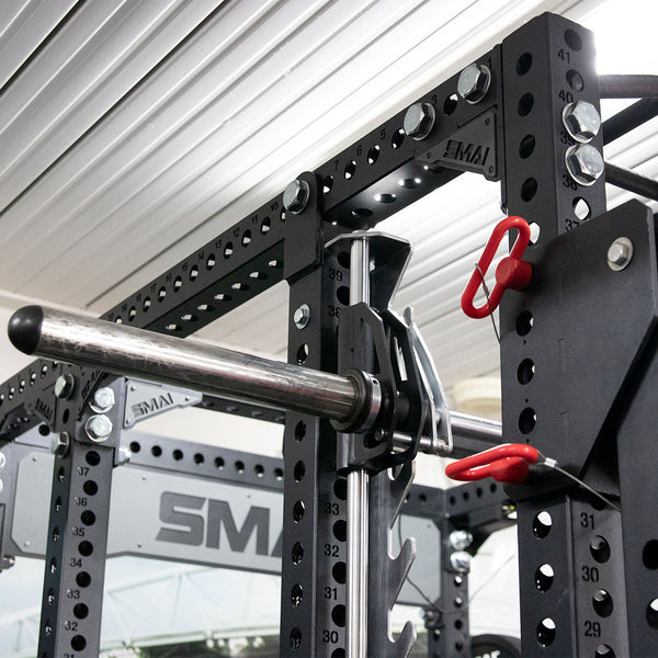 Close-up of a Smith Machine Insert from the Vanta Series by SMAI, featuring adjustable safety bars and weight pegs. Constructed from black metal, it includes numbered holes for height adjustments, set in an indoor gym designed for weightlifting enthusiasts.