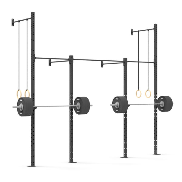 The Wall Mounted Rig - 2 Squat Cell with Bridge - X-Frame by No Sync To Channel Engine features two squat racks made from durable steel tubing, each supporting a barbell loaded with weights. Gymnastic rings hang elegantly from the structure. The sleek black equipment and wooden rings form a minimalist scene against a white backdrop, highlighting its modular design.