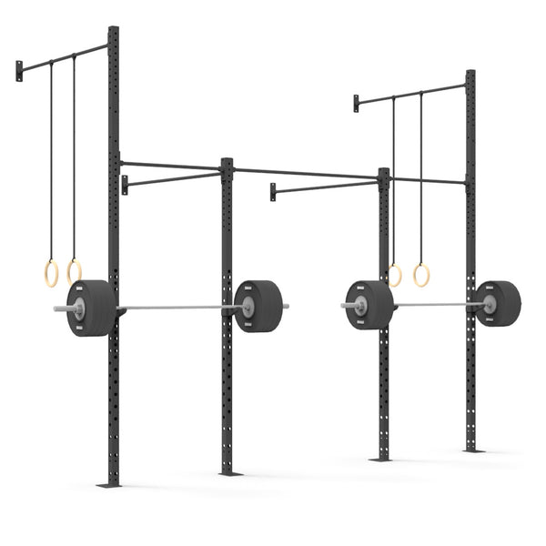 A gym setup includes the Wall Mounted Rig - 2 Squat Cell with Bridge - X-Frame, which features two parallel steel racks, each supporting a barbell with weights. Gymnastic rings are suspended from bars above the racks. This commercial equipment, supplied by No Sync To Channel Engine, is arranged against a plain white background to highlight its modular design for versatile workouts.