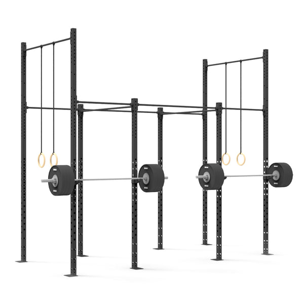 A gym setup featuring the "4 Squat Cell with Bridge" by No Sync To Channel Engine, showcasing a modular design with black steel tubing and two squat racks. Each rack holds a barbell with weights, while pairs of gymnastic rings hang from crossbars above. This commercial equipment structure is securely bolted to the ground.