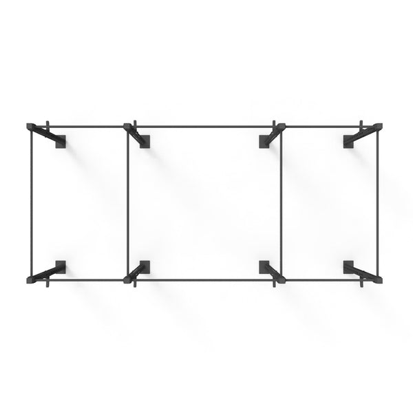 The Rig - 4 Squat Cells from SMAI is mounted on a white wall, featuring a minimalist design with an industrial look. This rectangular black metal wall shelf includes three open compartments, showcasing clean lines and visible bracket supports. It is crafted from steel tubing for enhanced durability and has a modular design.